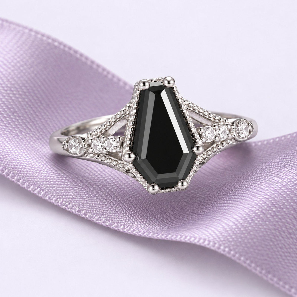 Lilith coffin-cut black onyx engagement ring with ornate white-gold shoulders rests on a continuous lavender silk ribbon.
