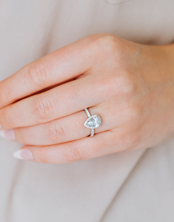 Hand wearing a diamond ring on a neutral background