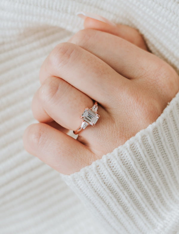 Hand wearing a diamond ring on a neutral background