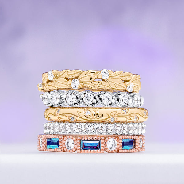 Stack of gold and silver rings with gemstones on a purple background