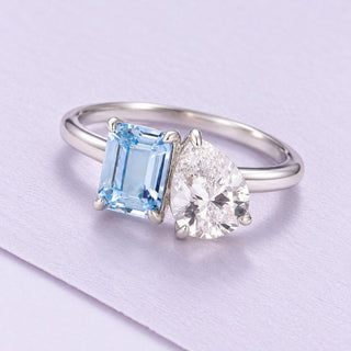 White-gold Toi Et Moi ring pairs an emerald-cut aquamarine with a pear lab-grown diamond on a large lilac paper sheet.