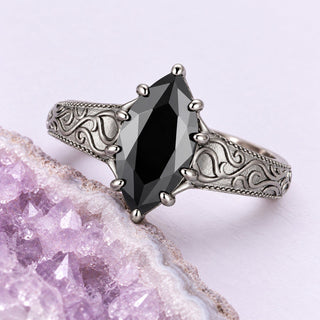 Marquise black onyx ring with engraved scrollwork, resting beside a pale lavender geode on a seamless lilac ground.