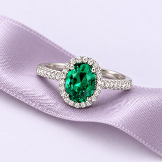 Oval green emerald ring with a delicate clear halo and white-gold pavé shoulders on a continuous dusty lavender ribbon.