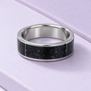 Men's tungsten ring with a broad black onyx inlay and polished edges resting naturally on full-size pale-lilac tiles.