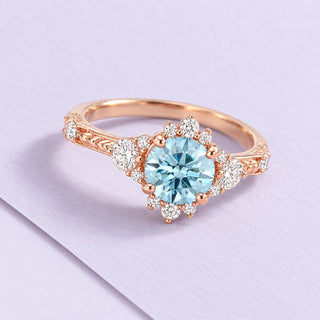 Rose-gold aquamarine ring with a round pale-blue center and clear accents, resting naturally on a large lilac paper sheet.