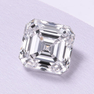 Asscher-cut loose diamond with concentric step facets, resting on fine lilac cotton paper in soft natural daylight.