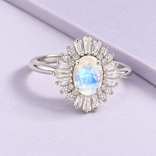 Victoria moonstone ring with a clear Art Deco halo and natural blue flash on broad pale-lilac tiles in soft daylight.