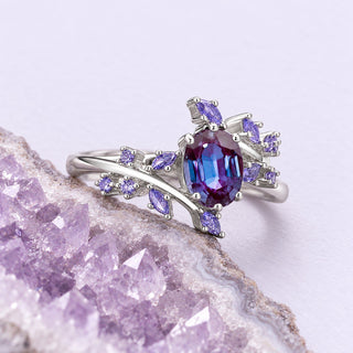 Silver alexandrite fairy leaf ring with lavender sapphire accents beside a cropped pale amethyst geode on lilac ground.