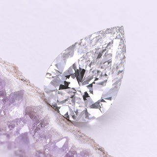 Pear-shaped loose lab-grown diamond resting beside a cropped lavender geode, shown in a close diagonal macro view.