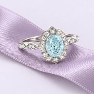 Pale-blue aquamarine ring with a scalloped diamond halo and white-gold infinity shoulders on continuous lavender silk.