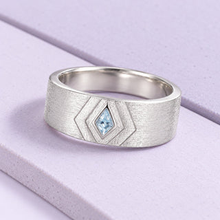 Brushed silver men's band with a kite aquamarine and geometric engraving on broad pale-lilac tiles in soft daylight.