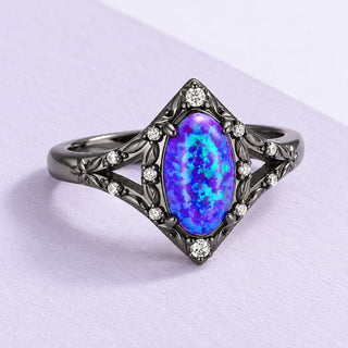 Nerida lavender opal ring in dark floral metalwork, resting on fine lilac paper under soft upper-left daylight.