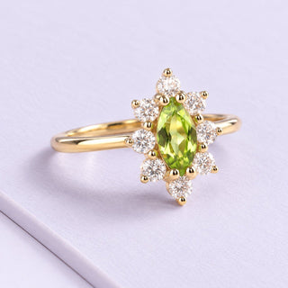 Marquise peridot ring in yellow gold with an airy clear-stone halo, resting naturally on pale lilac matte tiles.