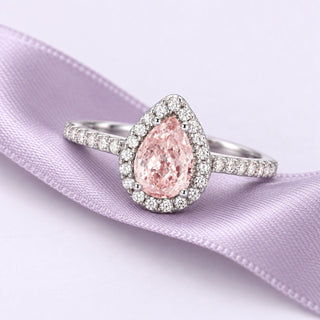 Blush-pink pear morganite halo ring in white gold resting on a broad dusty lavender silk ribbon in soft natural light.