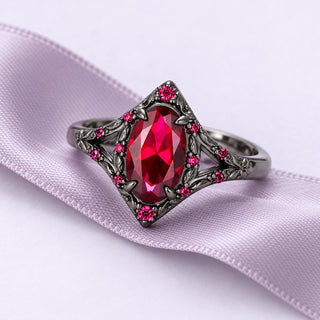 Nerida ruby ring in dark ornate metal with red accent stones, resting at a gentle angle on a long lavender silk ribbon.