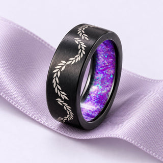 Black titanium wedding band with a laurel motif and lavender opal liner, resting naturally on broad lilac silk.