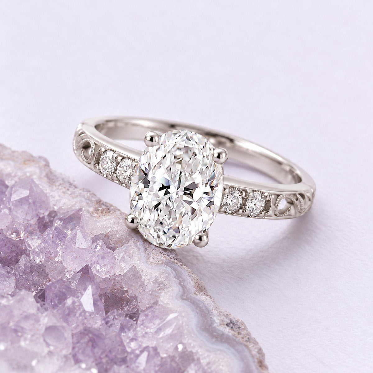 White-gold oval diamond filigree engagement ring resting beside a naturally cropped pale lavender amethyst geode.