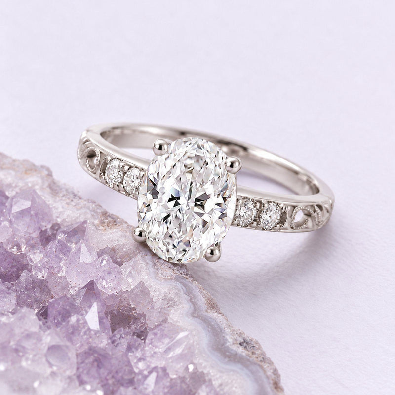 White-gold oval diamond filigree engagement ring resting beside a naturally cropped pale lavender amethyst geode.