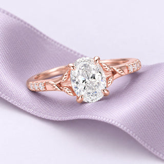 Rose gold leaf engagement ring with an oval diamond, resting on broad lavender silk against a pale lilac studio ground.