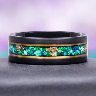 Black ring with green and gold inlay on a gray surface