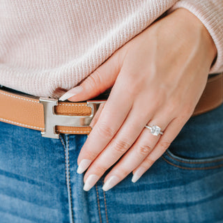Cushion cut diamond ring on a hand against a blue and pink background