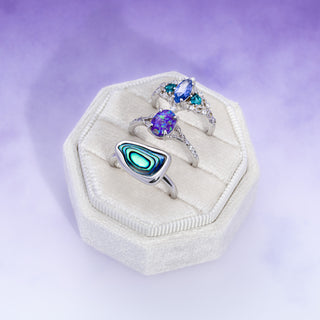 Three silver rings with gemstones in a white jewelry box on a purple background