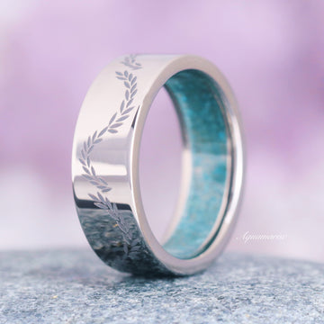 Titanium men's wedding ring with engraved design on a textured surface with a blurred purple background