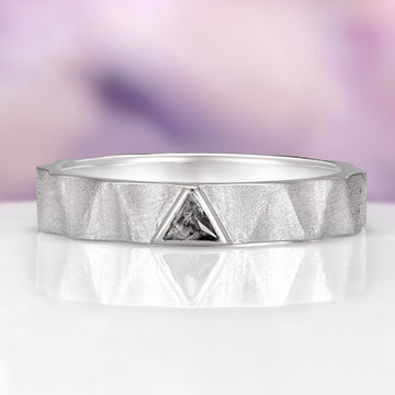 Silver ring with a diamond on a reflective surface and blurred purple background