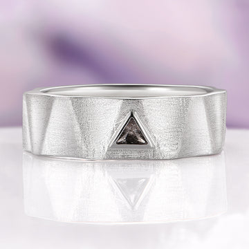 Silver ring with a triangle-shaped gemstone on a reflective surface with a blurred purple background