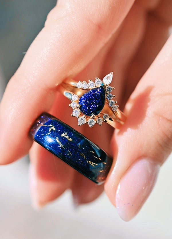 Close-up of a hand wearing two rings with blue gemstones and diamond accents.