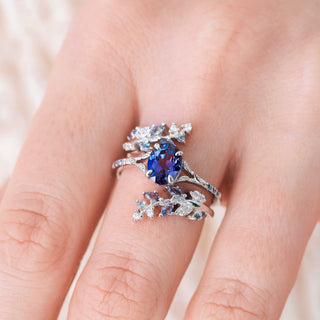 White gold ring with oval cut lab grown alexandrite center stone and diamond accents on hand over a light background
