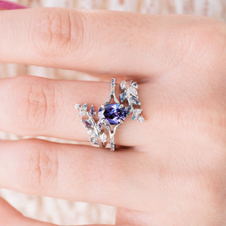 White gold ring with oval cut lab grown alexandrite center stone and diamond accents on hand over a light background