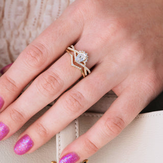 Yellow gold engagement ring set with teardrop diamond center stone and accents on hand over light background
