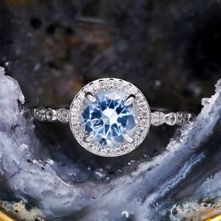 Art Deco Aquamarine Engagement Ring by Aquamarise, a round aquamarine with a diamond halo displayed against a dark geode.