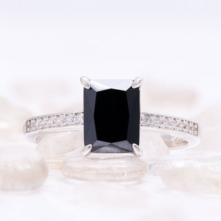 Close-up of the black onyx center stone and pavé sterling silver band resting on white river pebbles