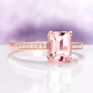Rose gold ring with a pink gemstone and diamond-studded band on a light purple background