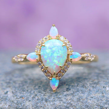 Blue Fire Opal Engagement Ring- 14K Solid Yellow Gold featuring a teardrop opal center with halo and pear-shaped opal accents in delicate yellow gold by Aquamarise Gold.