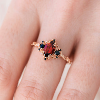 Rose gold engagement ring with oval cut natural garnet center stone and black onyx accents on hand over a light background 