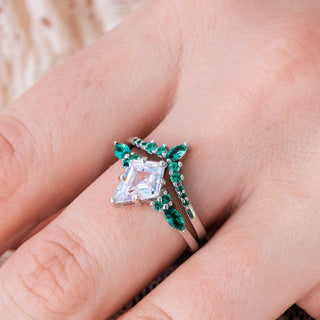White gold engagement ring set with kite cut diamond center stone and lab-grown emerald accents on hand over a light background  