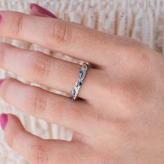 White gold wedding band with blue moissanite accents on hand over light background