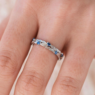 White gold wedding band with blue moissanite accents on hand over light background