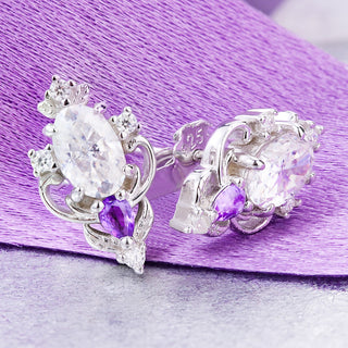 Carmilla moissanite and amethyst stud earrings on lilac satin, oval moissanite centers with pear amethyst drops and scroll frames