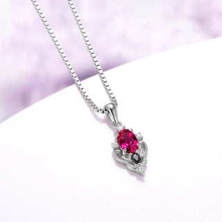 Angled view of the Carmilla ruby pendant showing the tapered bail, carved scroll frame and sterling silver box chain