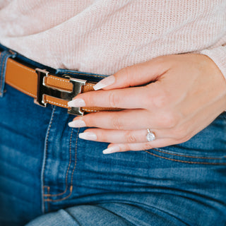 Cushion cut diamond ring on a hand against a blue and pink background