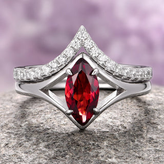 A marquise-cut red garnet ring with a chevron band, set in 14K white gold, displayed on a rock.