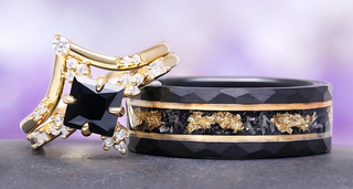 Two rings, one gold and black with a star-shaped gem, the other black with gold accents, on a gray surface with a purple gradient background.
