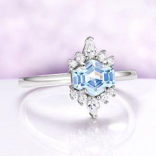 Elegant ring with a blue gemstone and diamond accents on a soft purple background