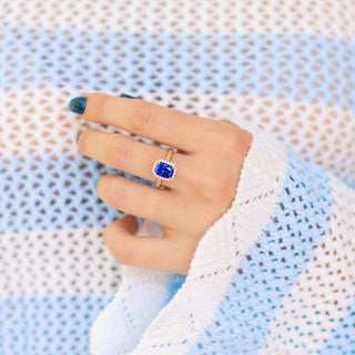 Blue Sapphire Engagement Ring Cushion Cut Ceylon Sapphire on hand over textured blue and white background
