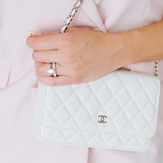 Solitaire diamond ring and band on a hand holding a white purse against a pink background 