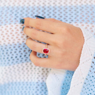 Ruby Engagement Ring Cushion Cut Ruby Halo Ring on hand over textured blue and white background